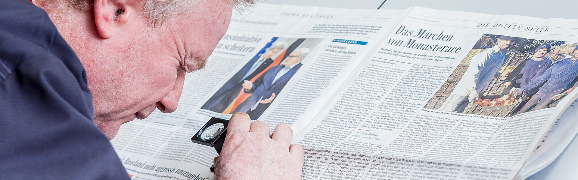 Nahaufnahme einer Person die das Layout einer Zeitung mit einer Lupe überprüft