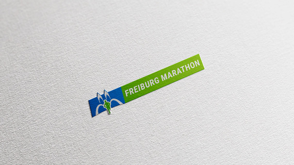 Ansicht des Logos von Freiburg Marathon neu in Farbe auf Hellgrau und Papier
