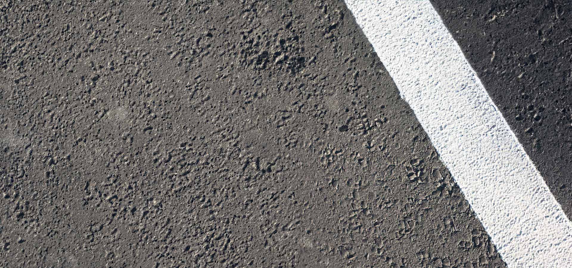 Nahaufnahme einer rauen Asphaltoberfläche mit einer einzelnen, weiß gemalten Linie, die diagonal durch das Bild verläuft