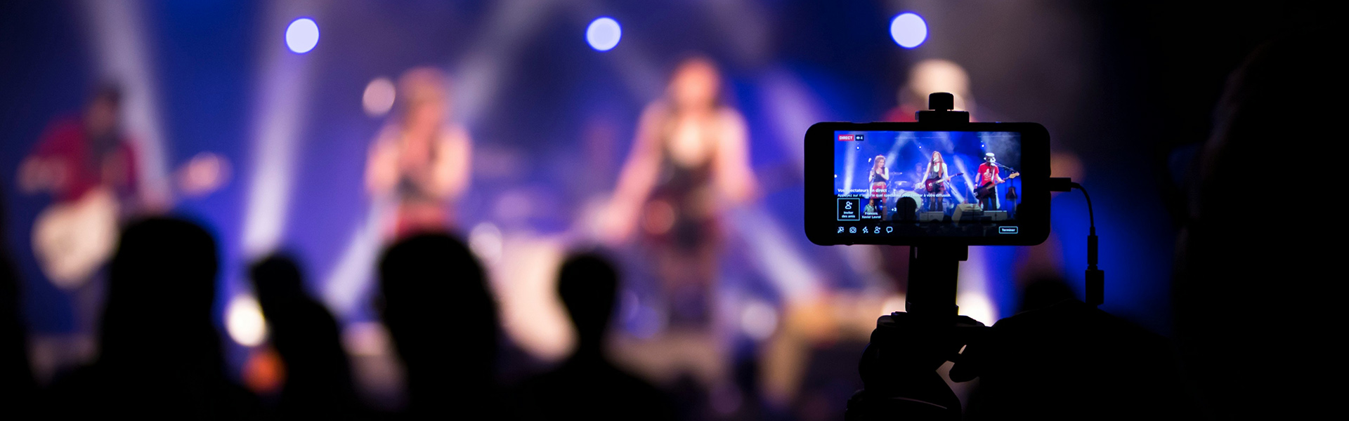 Smartphone im Querformat welches ein Konzert aufnimmt, während das eigentliche Konzert im Hintergrund unscharf ist