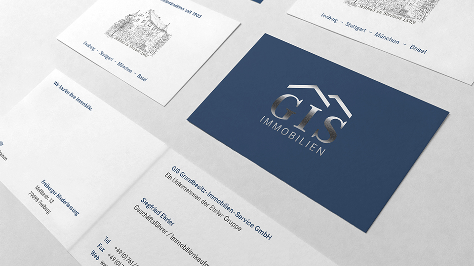 Ansicht Vorder- und Rückseite mehrerer Visitenkarten von GIS Immobilien auf weißem Tisch