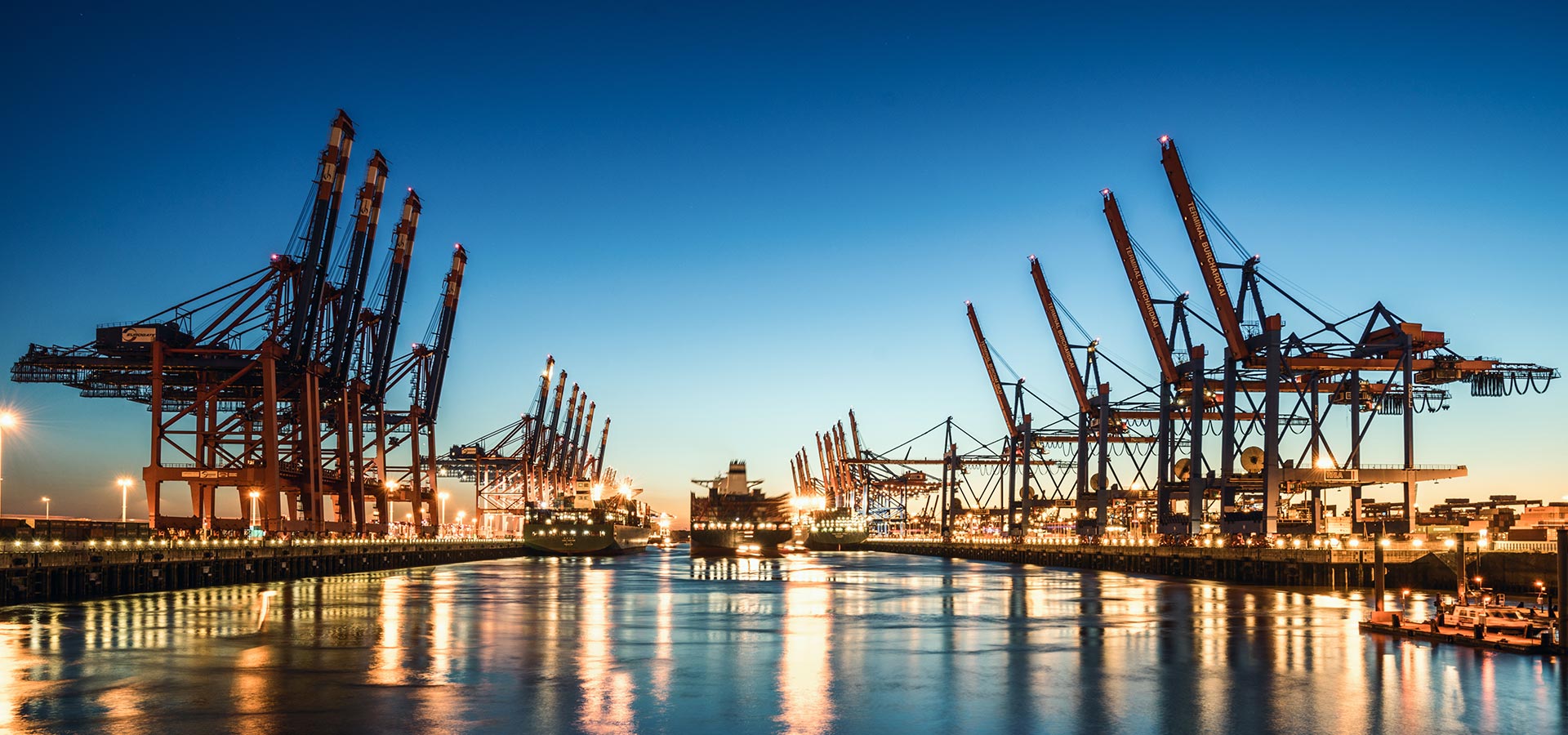 Nächtliche Ansicht eines Hafens mit großen Schiffskränen auf beiden Seiten und einem Containerschiff in der Mitte