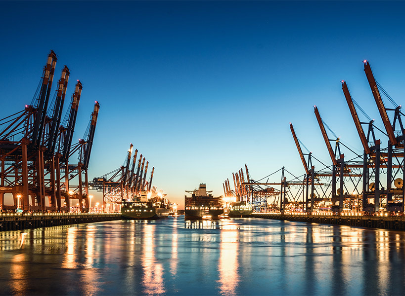 Nächtliche Ansicht eines Hafens mit großen Schiffskränen auf beiden Seiten und einem Containerschiff in der Mitte