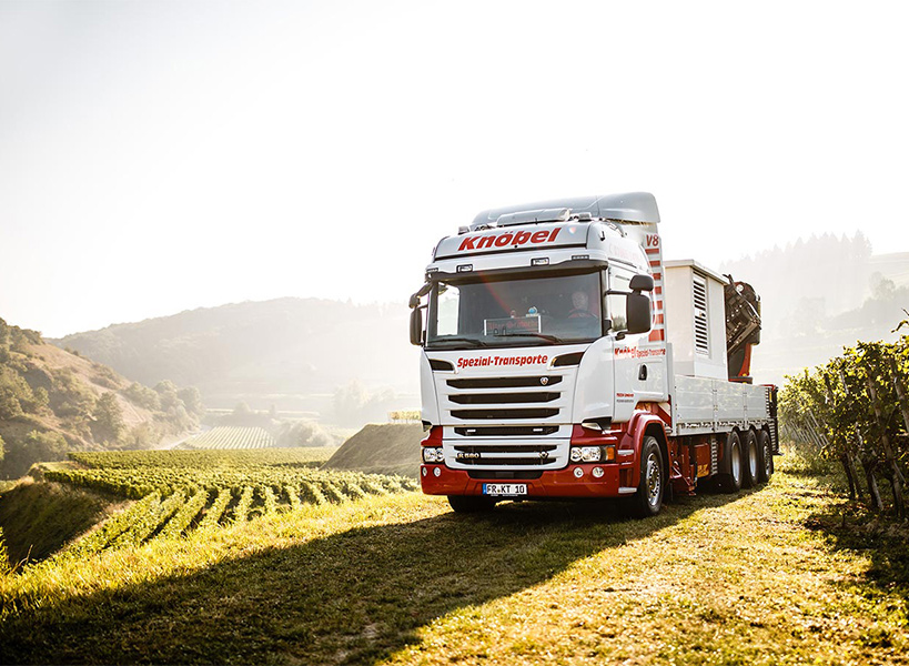 Rot-weißer LKW von Knöbel steht auf einer Wiese in der Nähe eines Weinbergs