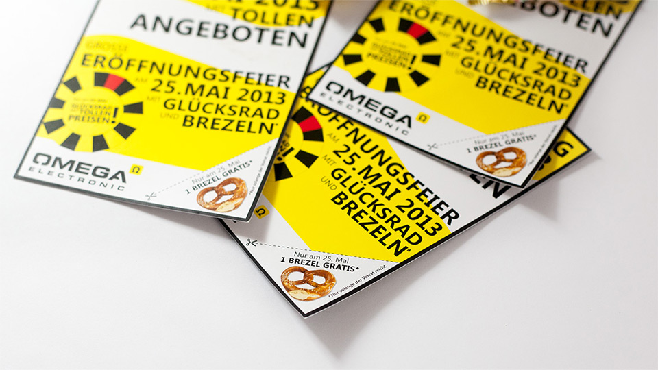 Nahaufnahme dreier Flyer im Corporate Design von Omega Electronics auf einem weißen Tisch
