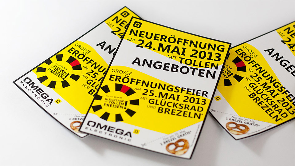 Nahaufnahme dreier Flyer im Corporate Design von Omega Electronics auf einem weißen Tisch