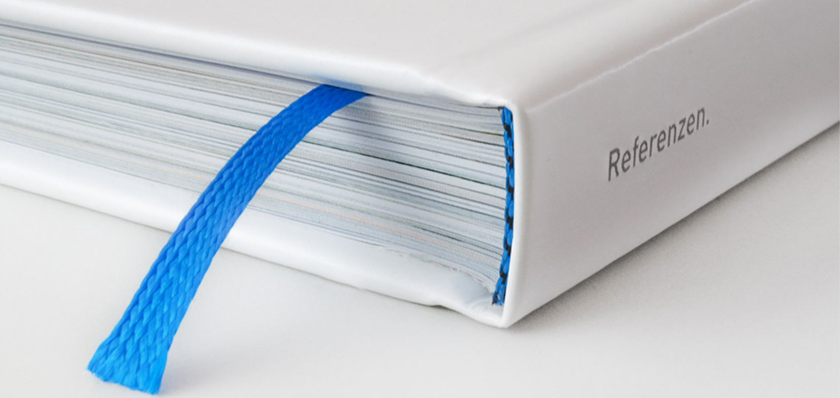 Nahaufnahme eines hochwertig gebundenen, weißen Buchrücken im Hardcover mit blauem Leseband
