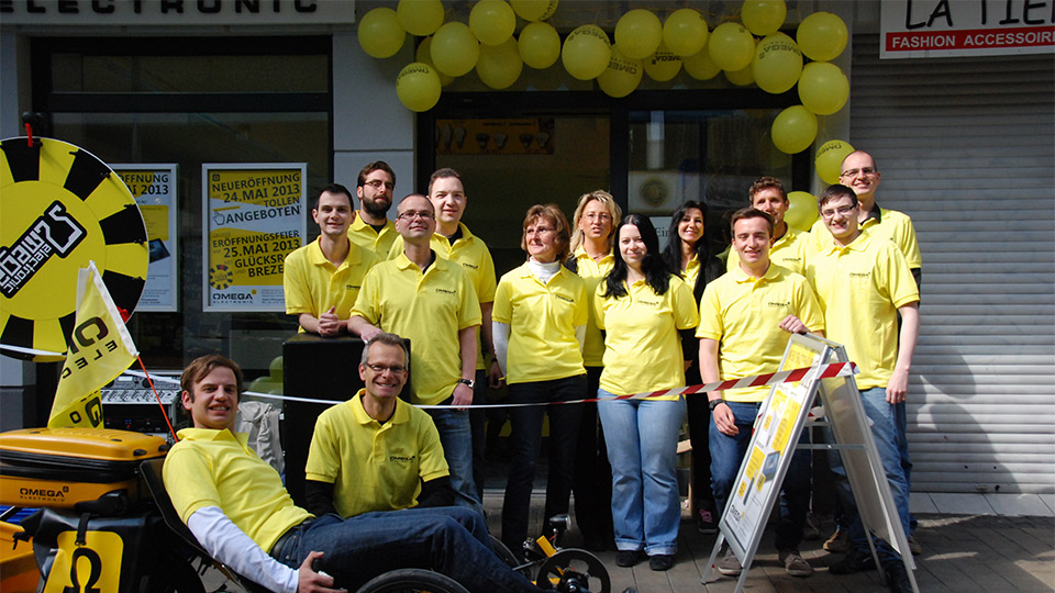 Gruppenbild der Mitarbeiter von Omega Electronics vor der Filiale in Mitarbeiterkleidung